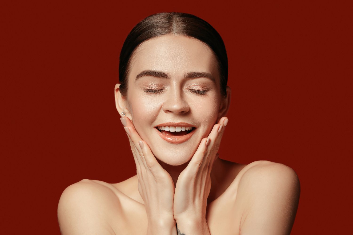 A woman is smiling and touching her face with her hands.