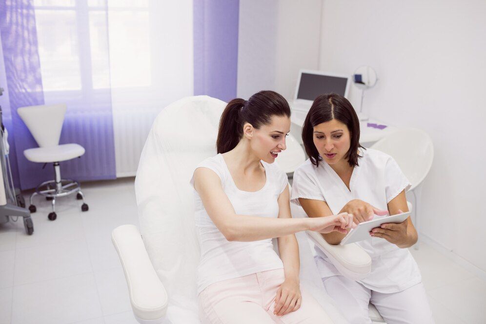 A woman is sitting in a chair while a nurse looks at a tablet.