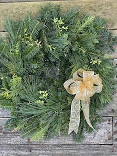 A christmas wreath with a gold bow is sitting on a wooden table.