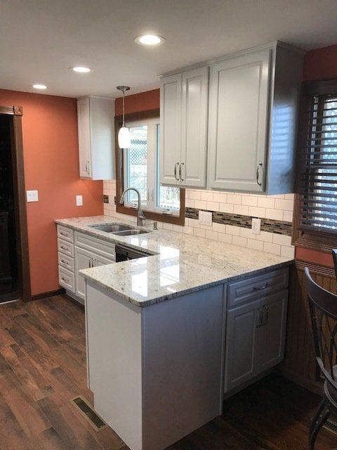 A kitchen with white cabinets , marble counter tops , a sink and a window.