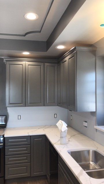 A kitchen with gray cabinets and a stainless steel sink