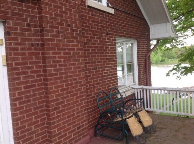 A brick building with a bench and chairs on the porch.