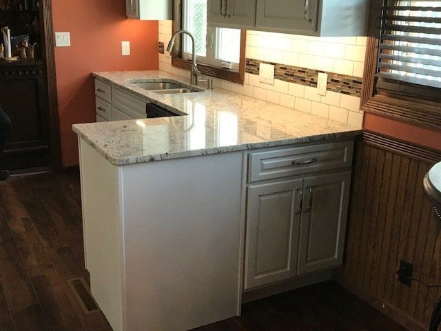 A kitchen with white cabinets , granite counter tops , a sink and a window.