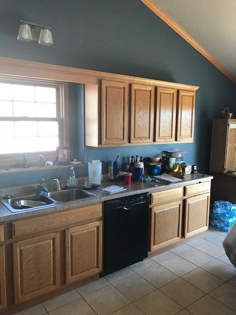 A kitchen with wooden cabinets , a sink , and a black dishwasher.