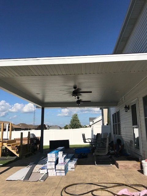 A white house with a covered patio with a ceiling fan.