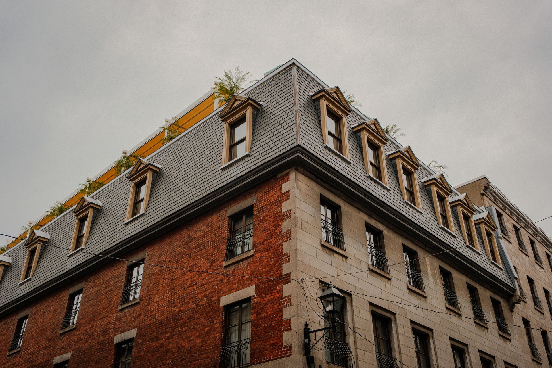 Bâtiment en brique et pierre avec toit mansardé gris et lucarnes ; ciel nuageux.