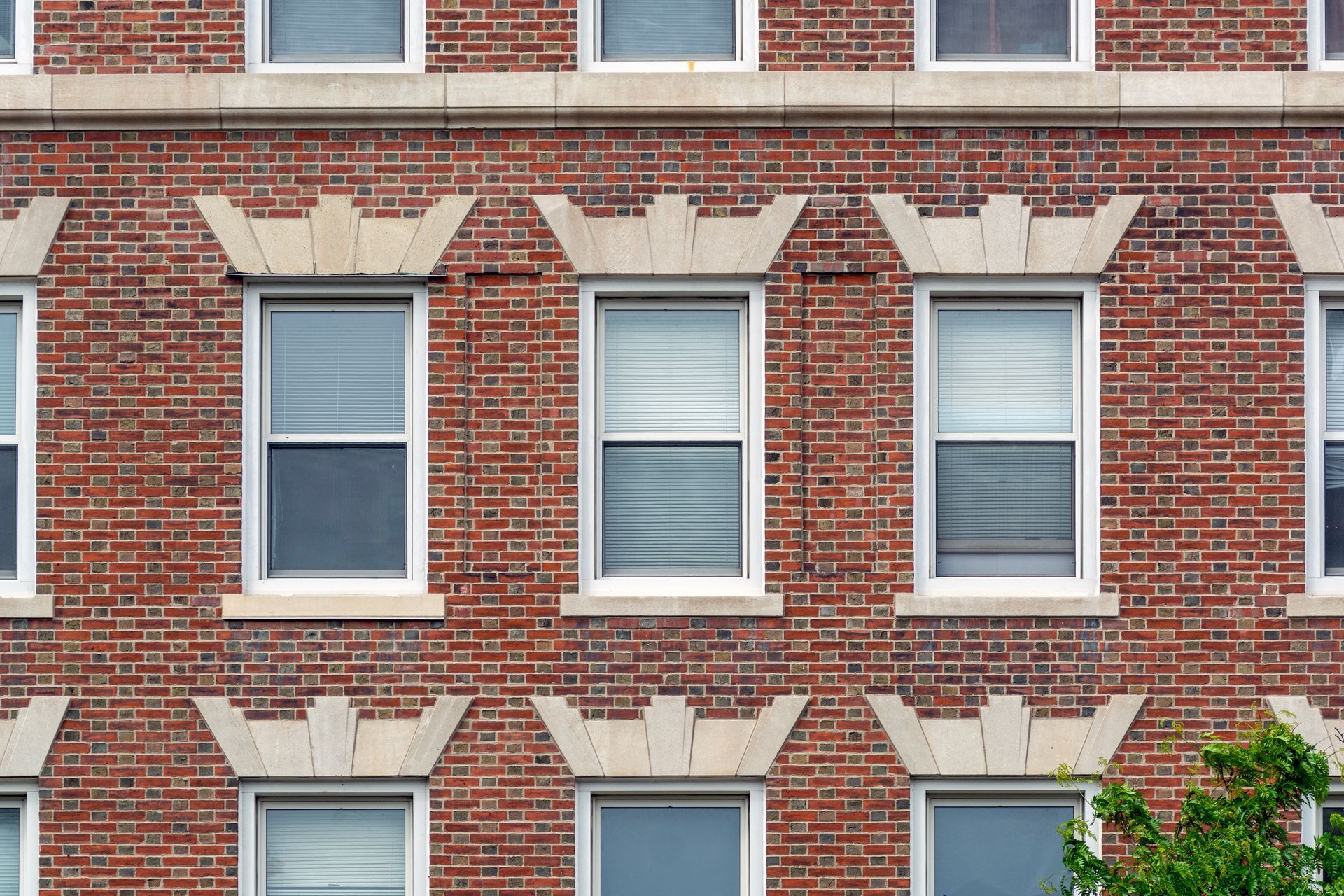 Façade de bâtiment en briques avec rangées de fenêtres ; ornements en pierre au-dessus de chaque fenêtre.
