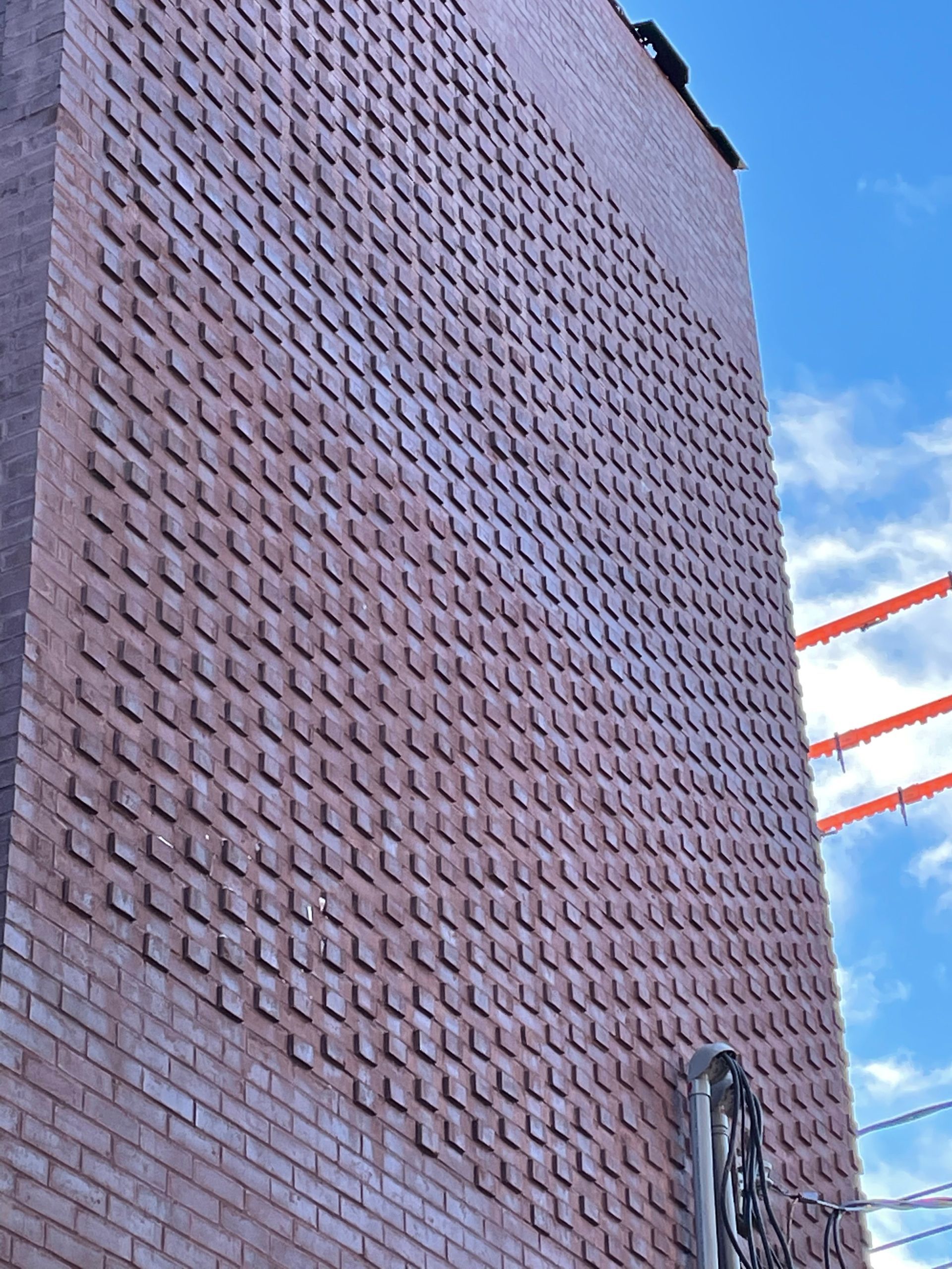 Bâtiment en briques avec une façade à motifs, sur fond de ciel bleu partiellement nuageux.