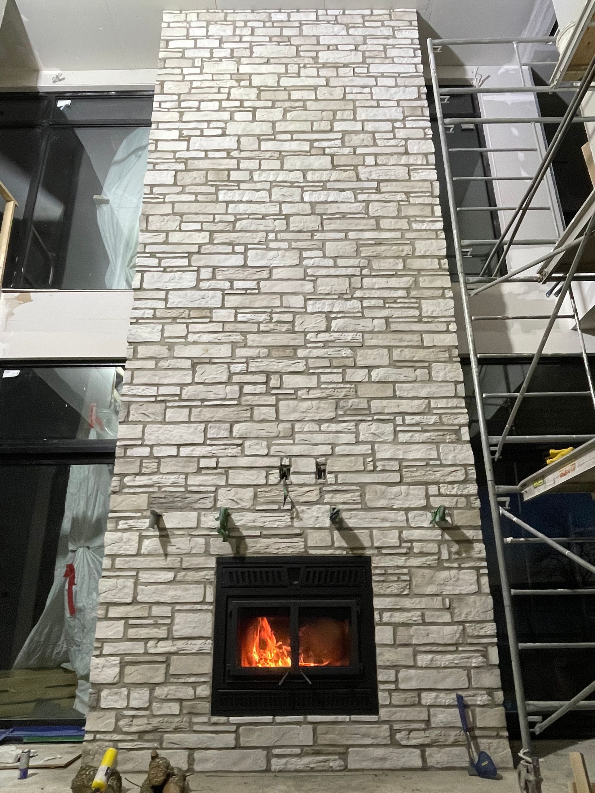 Cheminée en pierre avec feu allumé, installée sur un mur à deux étages. Échafaudage sur le côté.