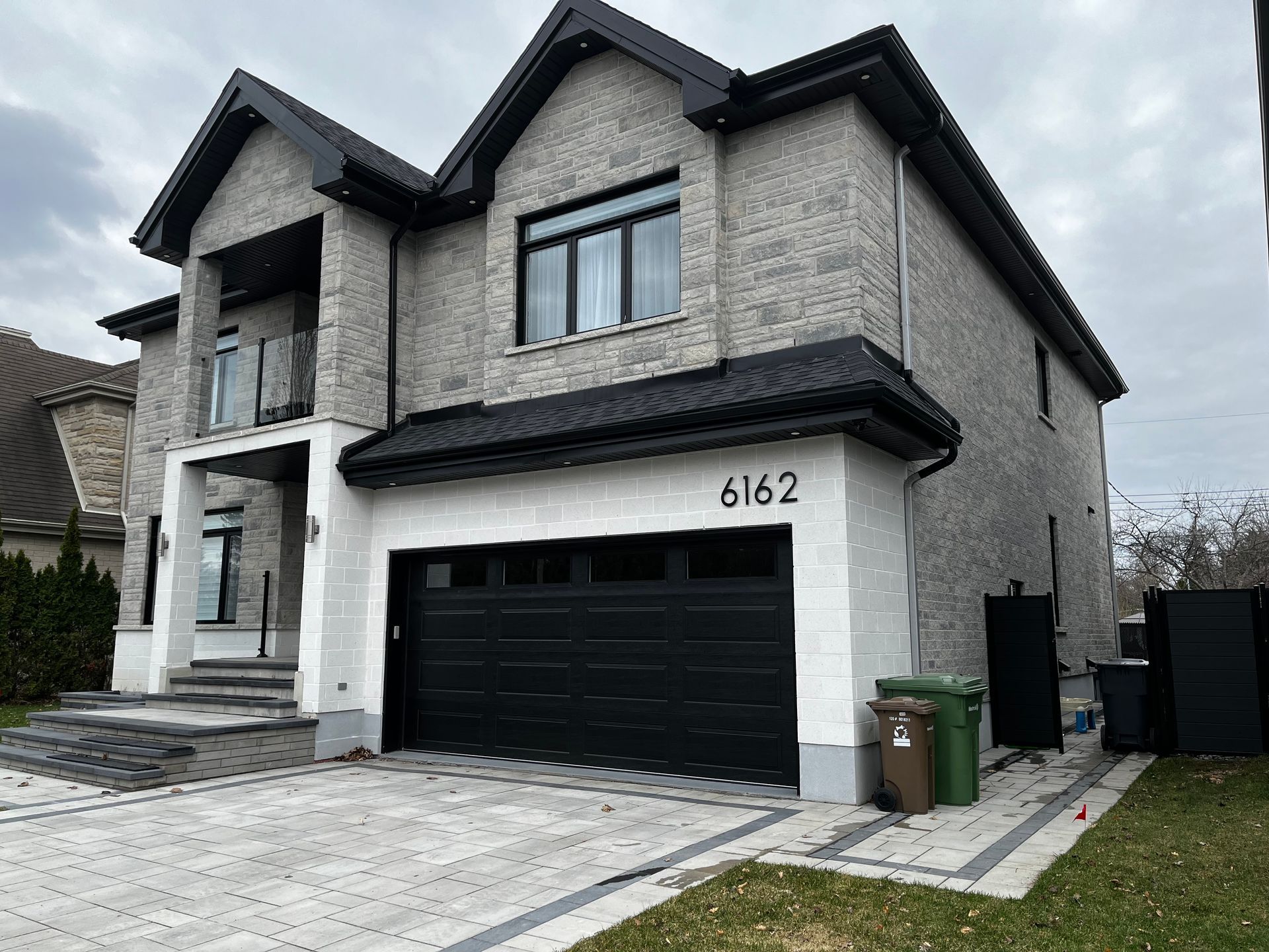Maison moderne en briques à deux étages avec porte de garage noire, marches et adresse 6162.