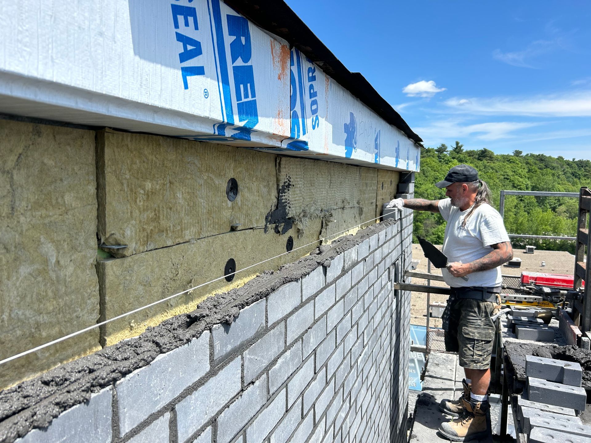 Un maçon pose des briques sur l'extérieur d'un bâtiment, guide-fil visible.