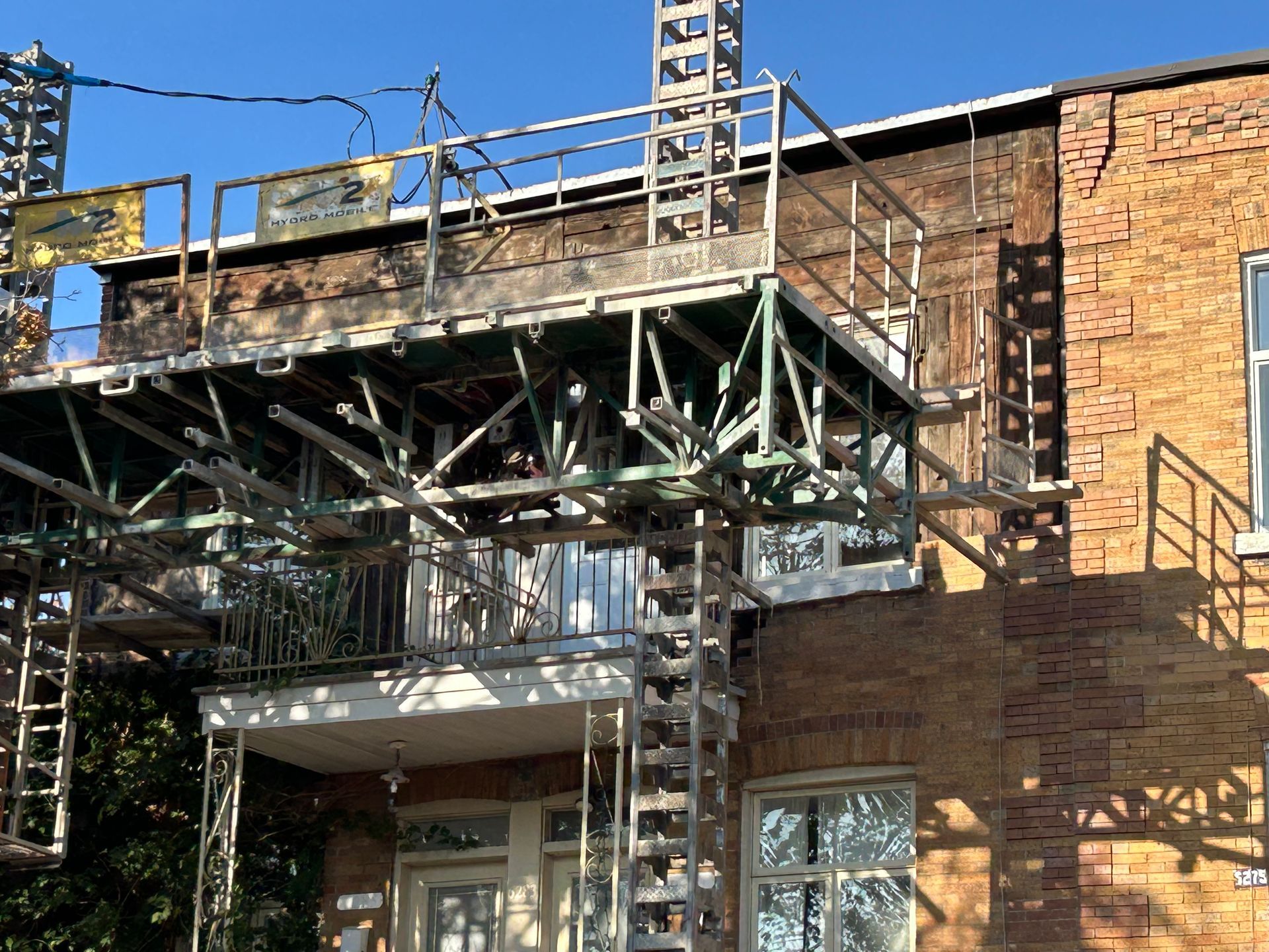 Échafaudage sur l'extérieur d'un bâtiment en briques pour des réparations ; structure métallique, lumière du soleil, fenêtres et porte.