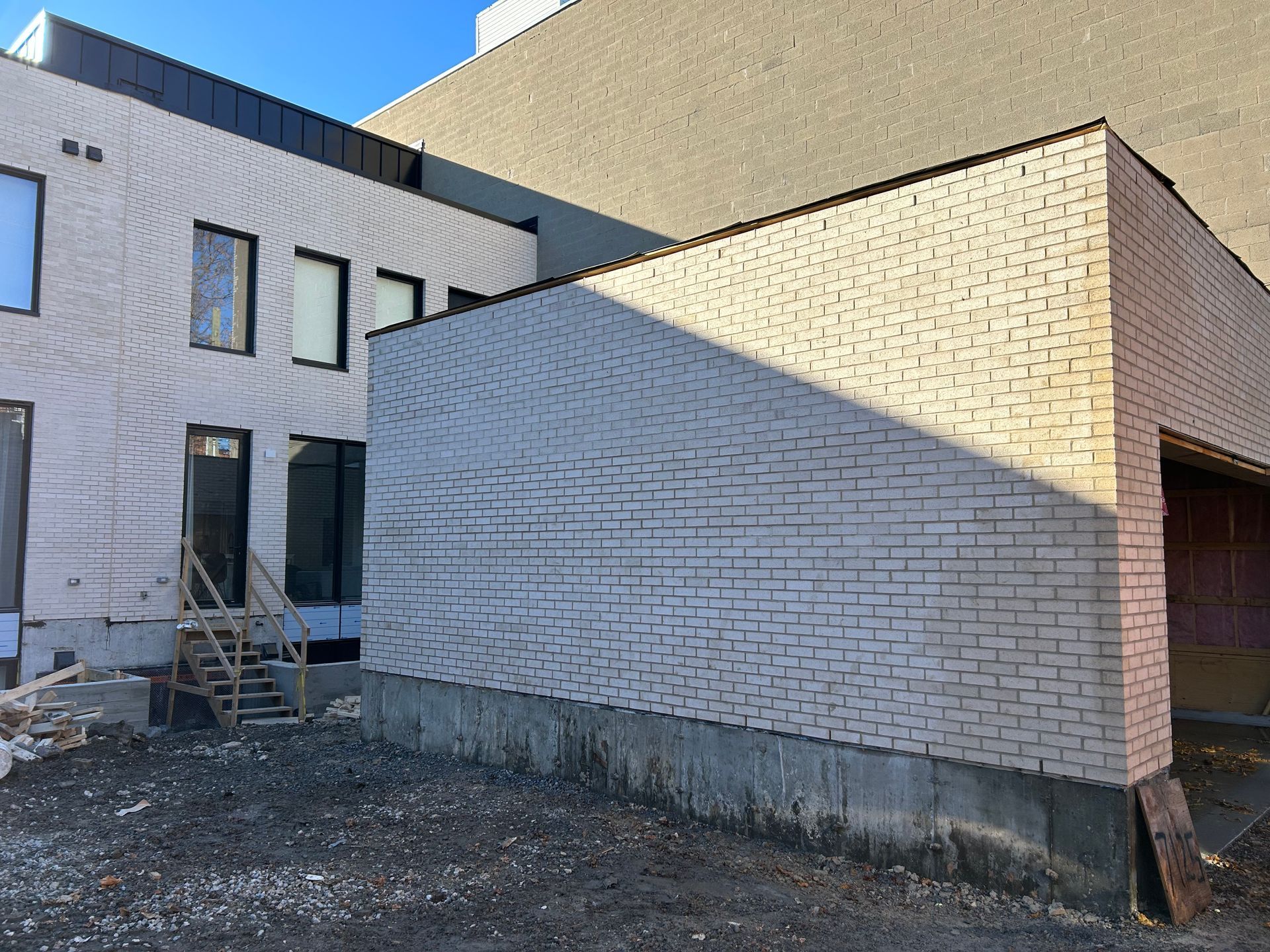 Bâtiment de deux étages avec murs en briques claires, ombres projetées par le soleil et fondations exposées.