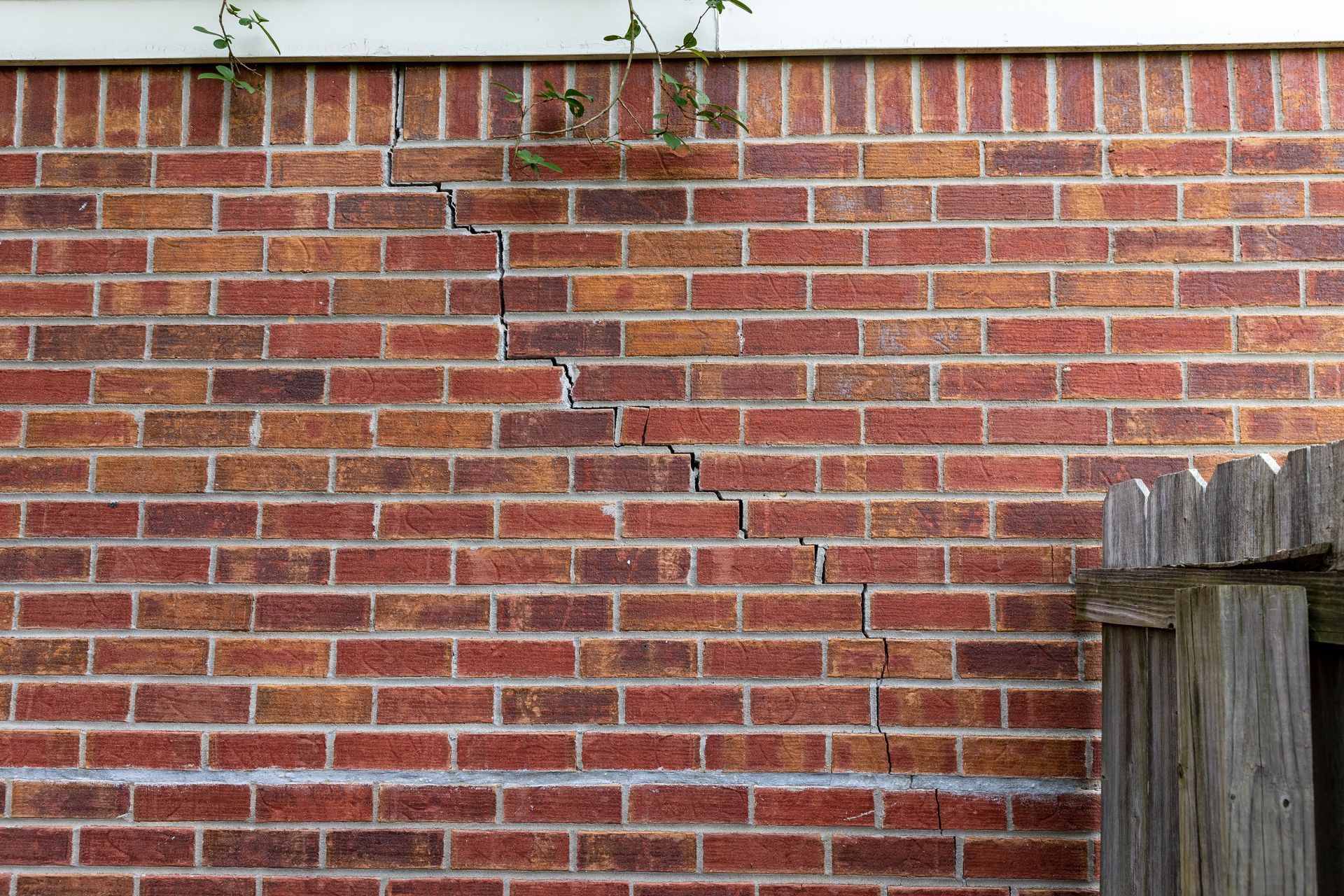 Mur de briques avec une grande fissure déchiquetée qui court verticalement.