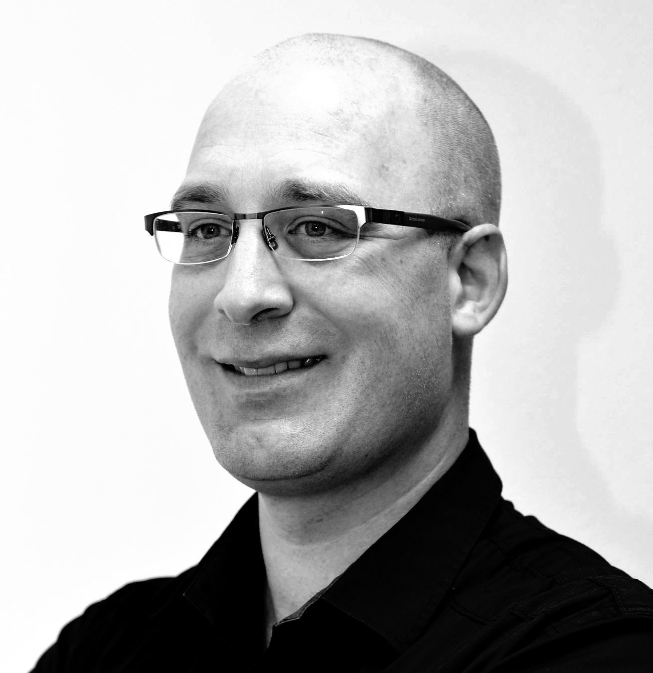 Een kale man met een bril en een zwart shirt