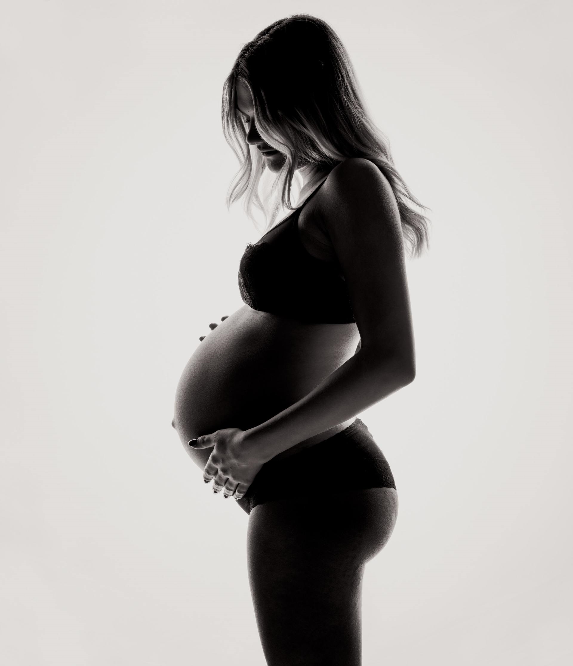 Een zwart-witfoto van een zwangere vrouw die haar buik vasthoudt.