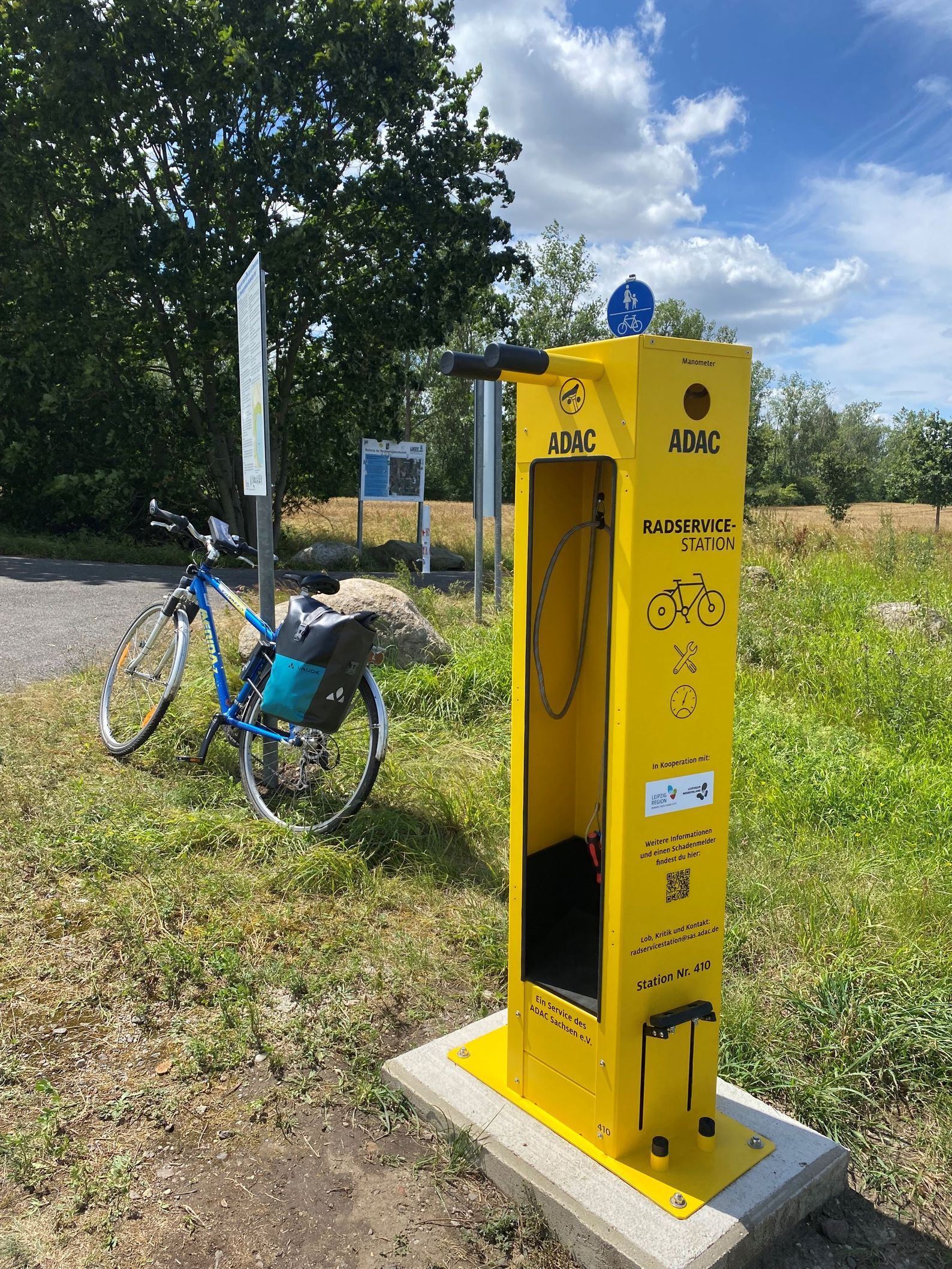 ADAC-Radservicestation als gelbe Säule mit Werkzeug und Luftpumpe, daneben steht ein Fahrrad