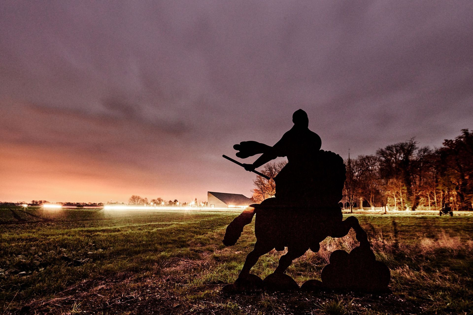 Schlachtfeldpfad in Lützen, kämpfender Reiter vor beleuchtetem Museum in Lützen in der Dämmerung