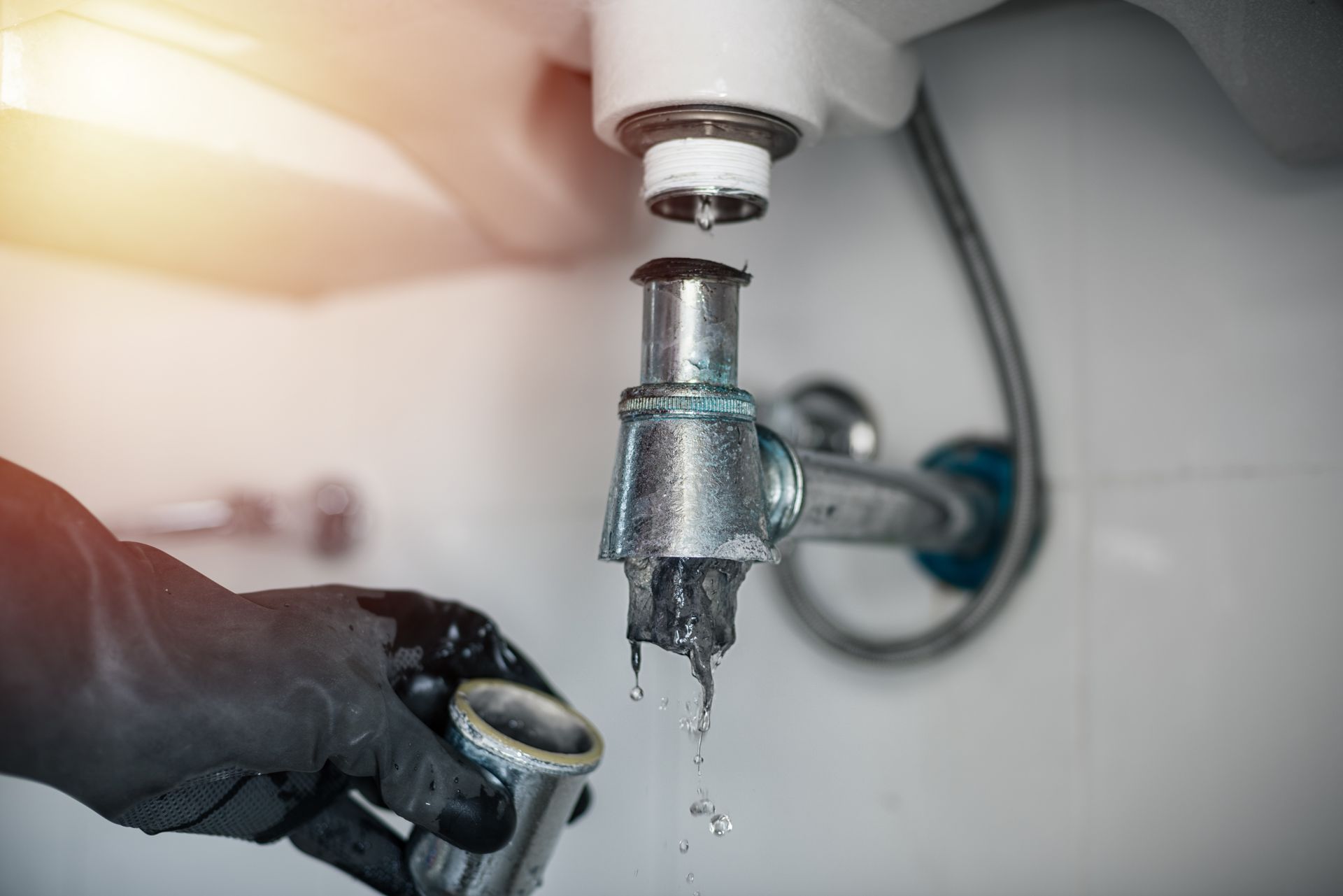 Emergency plumber removing a dirty, clogged drain trap under a home basin.