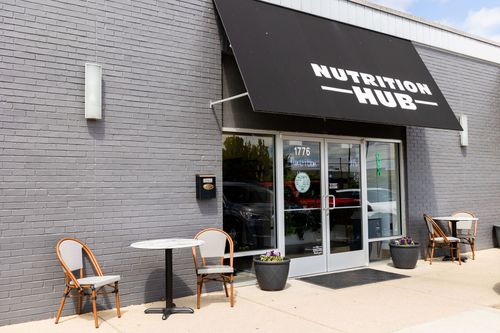 A brick building with a black awning over the door and tables and chairs outside.