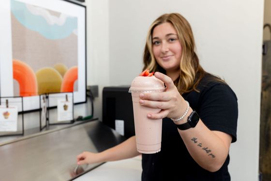 A woman is holding a strawberry milkshake in her hand.