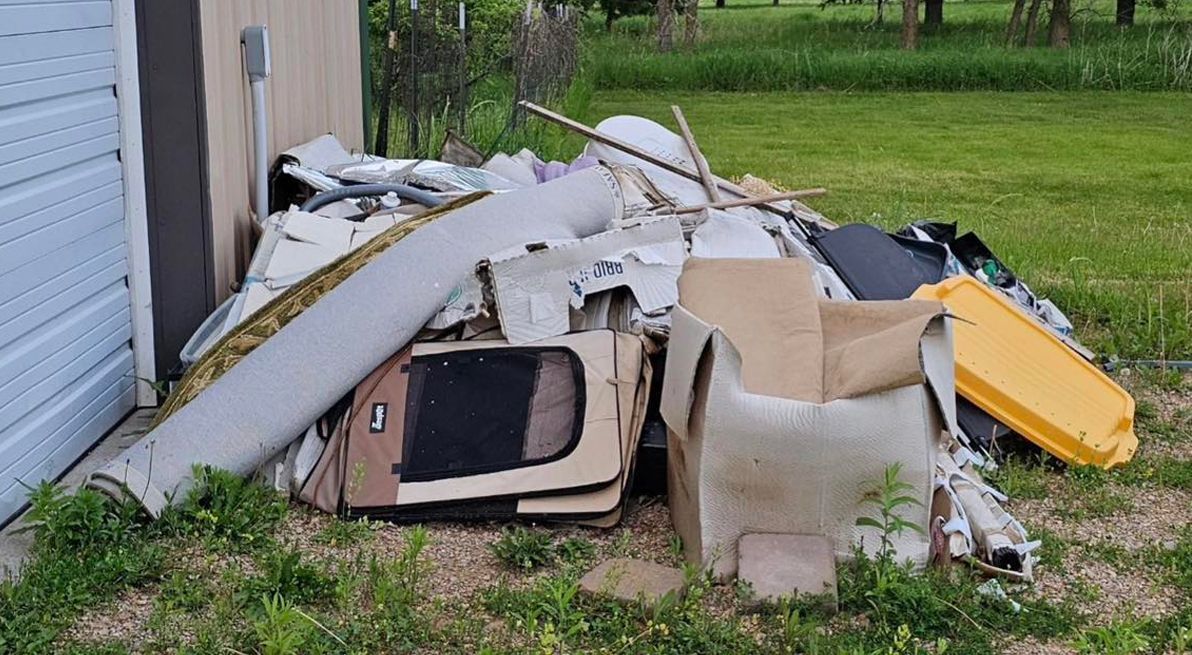 A pile of trash is sitting in the grass in front of a garage door.