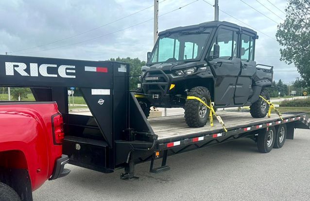 A red truck is towing a black atv on a trailer.