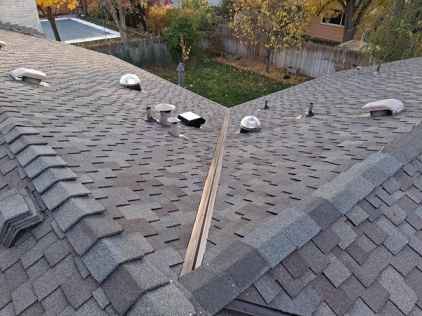 Overhead view of a roof with gray asphalt shingles and several ventilation pipes.