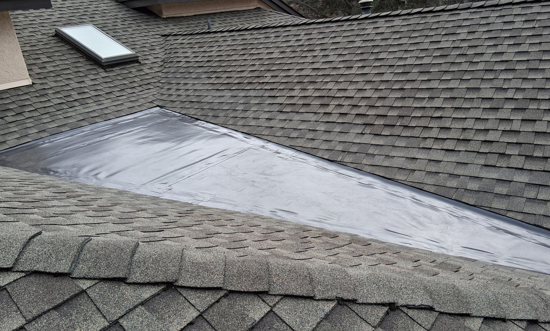 Close-up of a gray shingled roof with a dark, flat surface area, possibly sealed for weather protection.