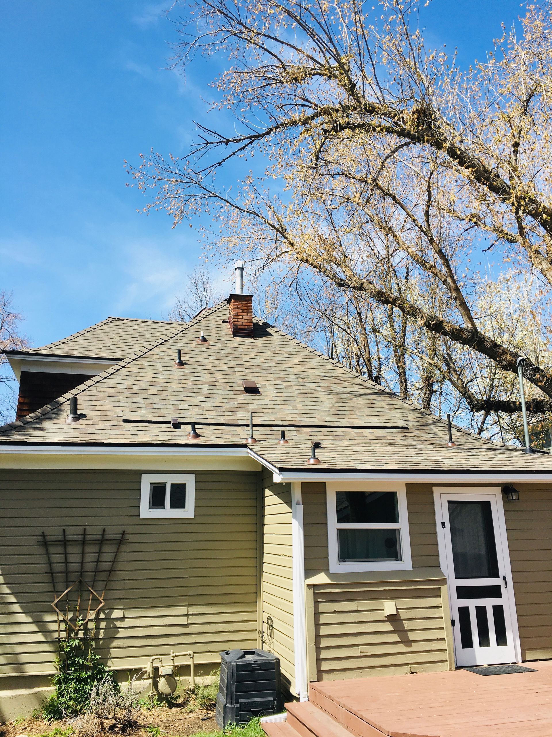House exterior with chimney, roof, windows, and a partially visible tree under a blue sky.
