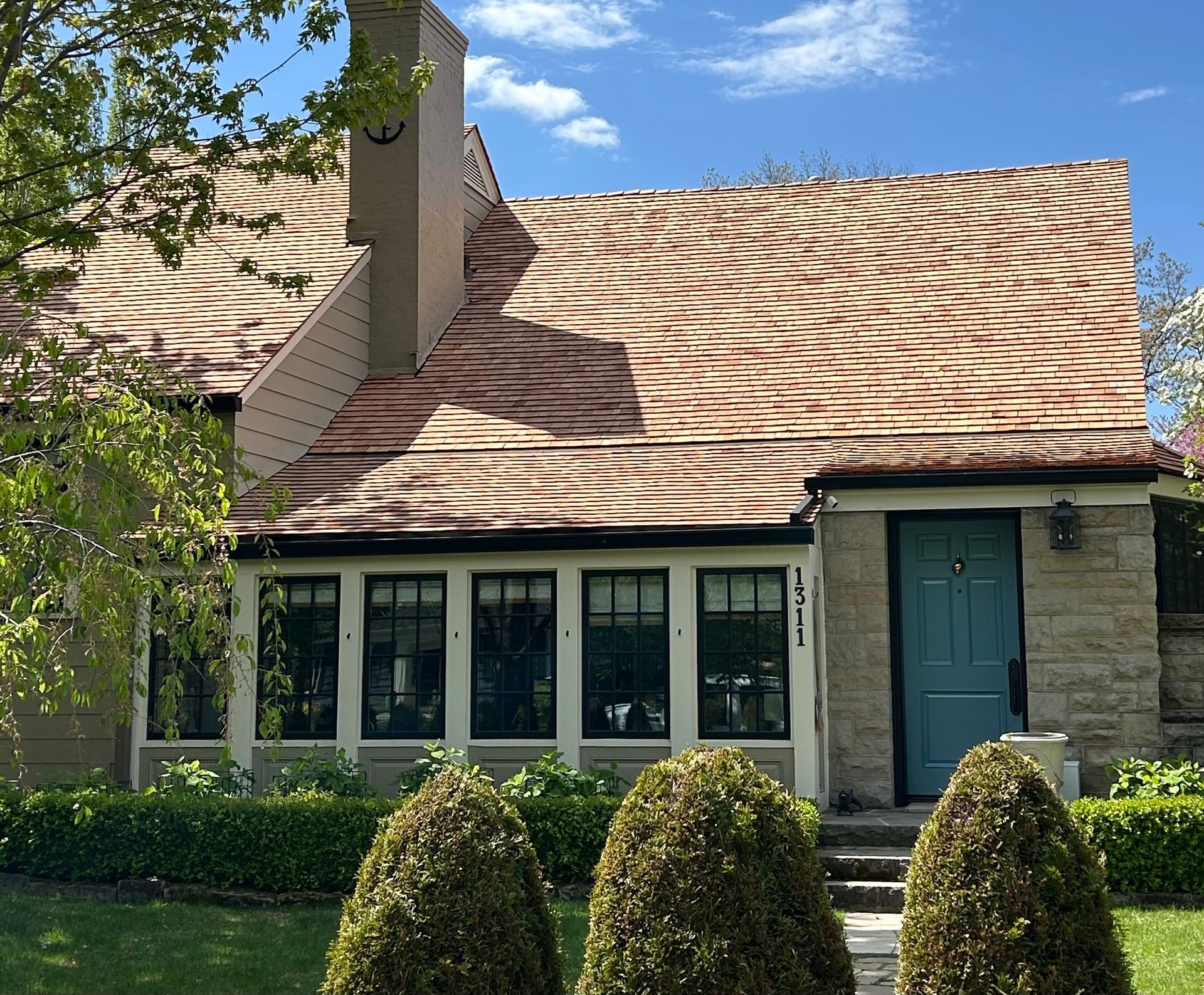 House with textured brown and tan roof, teal door, stone facade, and manicured landscaping.