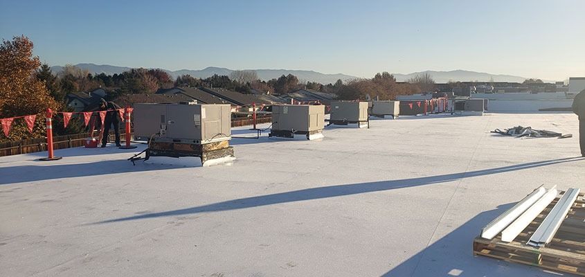 A rooftop with several square vents, workers, and some equipment. Clear blue sky, daytime.