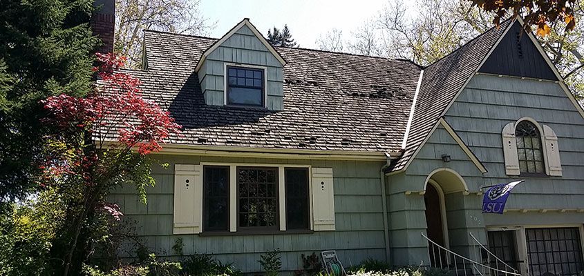A pale blue house with a dark roof, shutters, and a small window in the upper center.