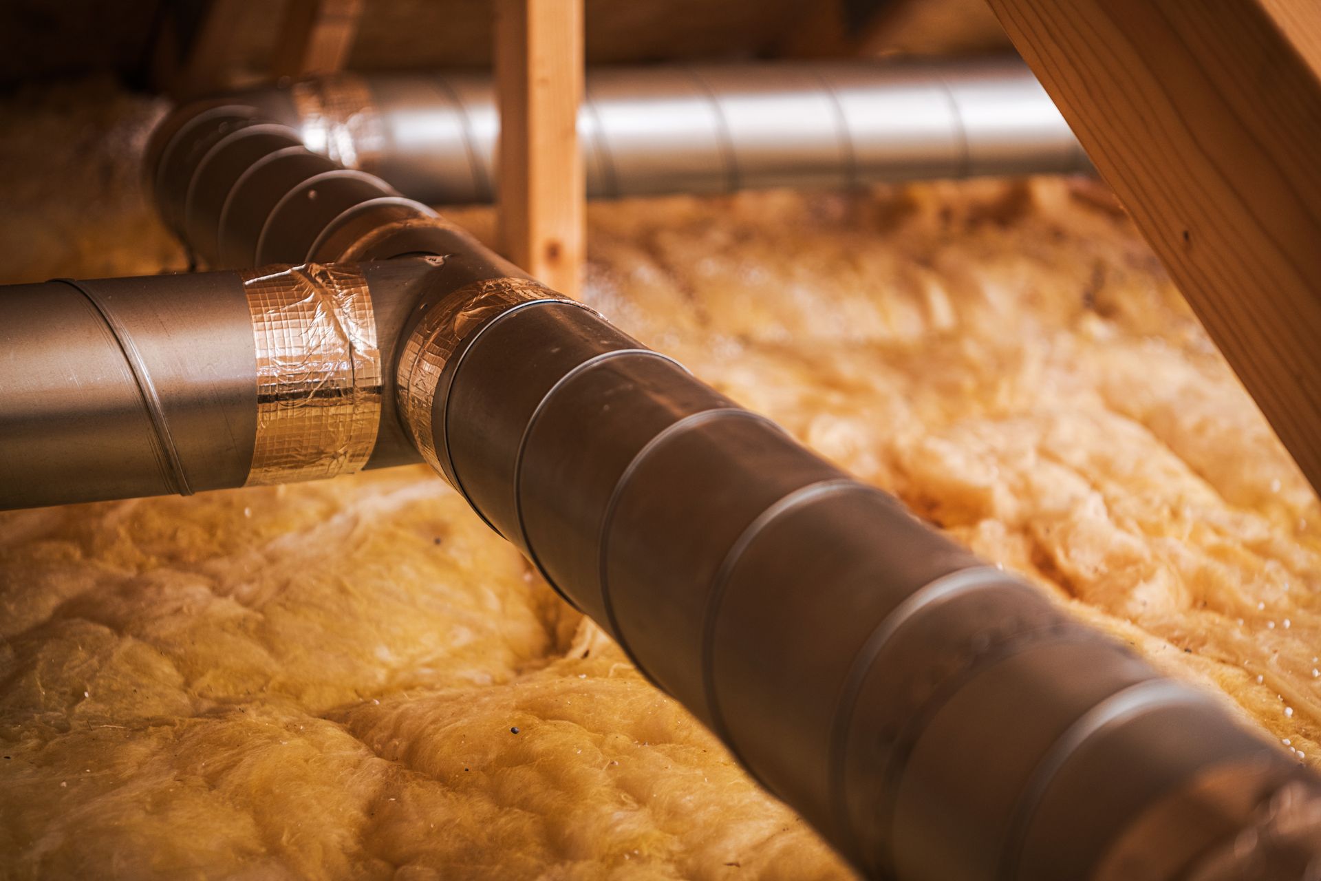 Insulated HVAC ductwork in an attic, running through insulation and between wooden beams.