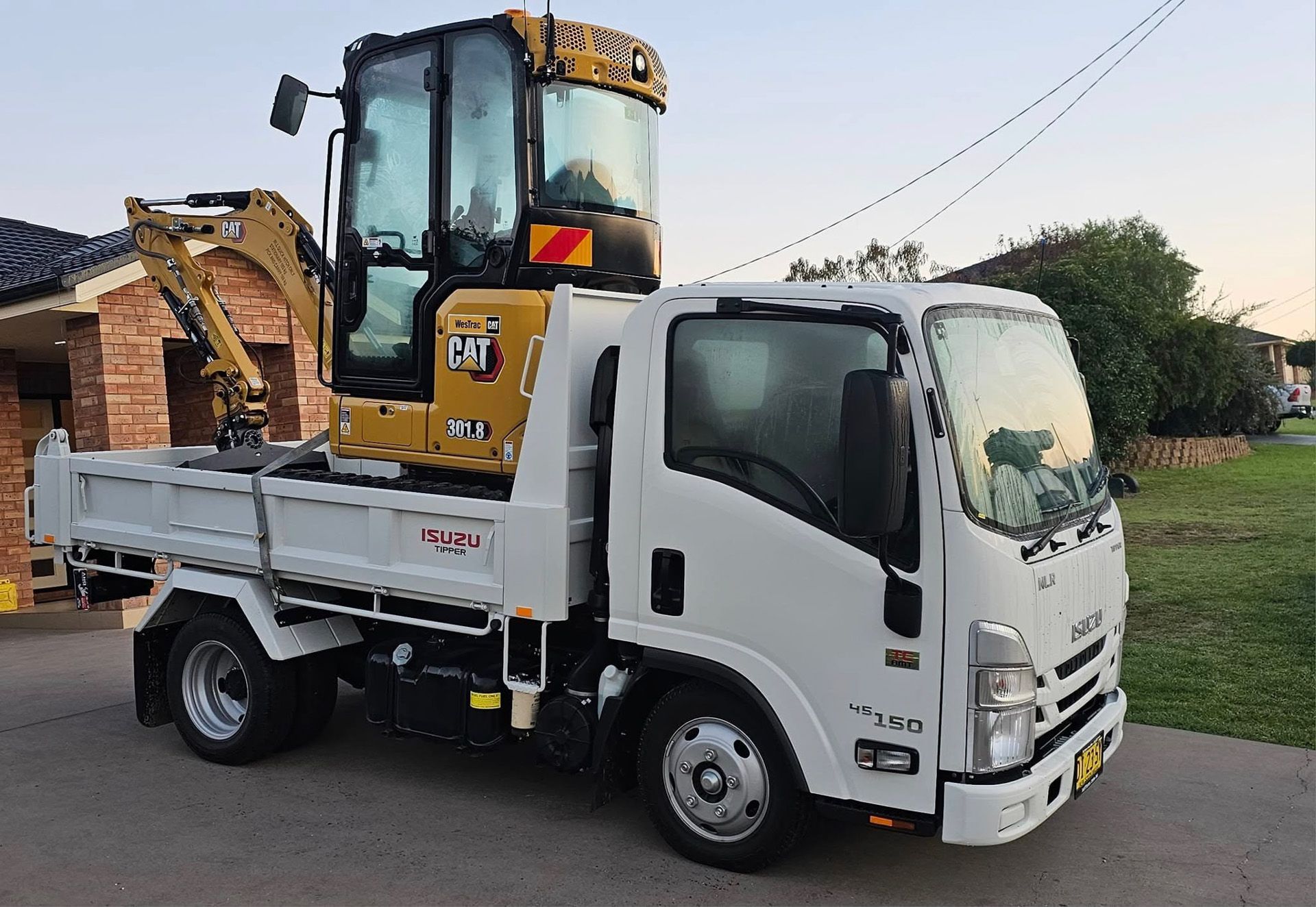 Yellow excavator on a flatbed trailer attached to a yellow semi-truck, parked outdoors.