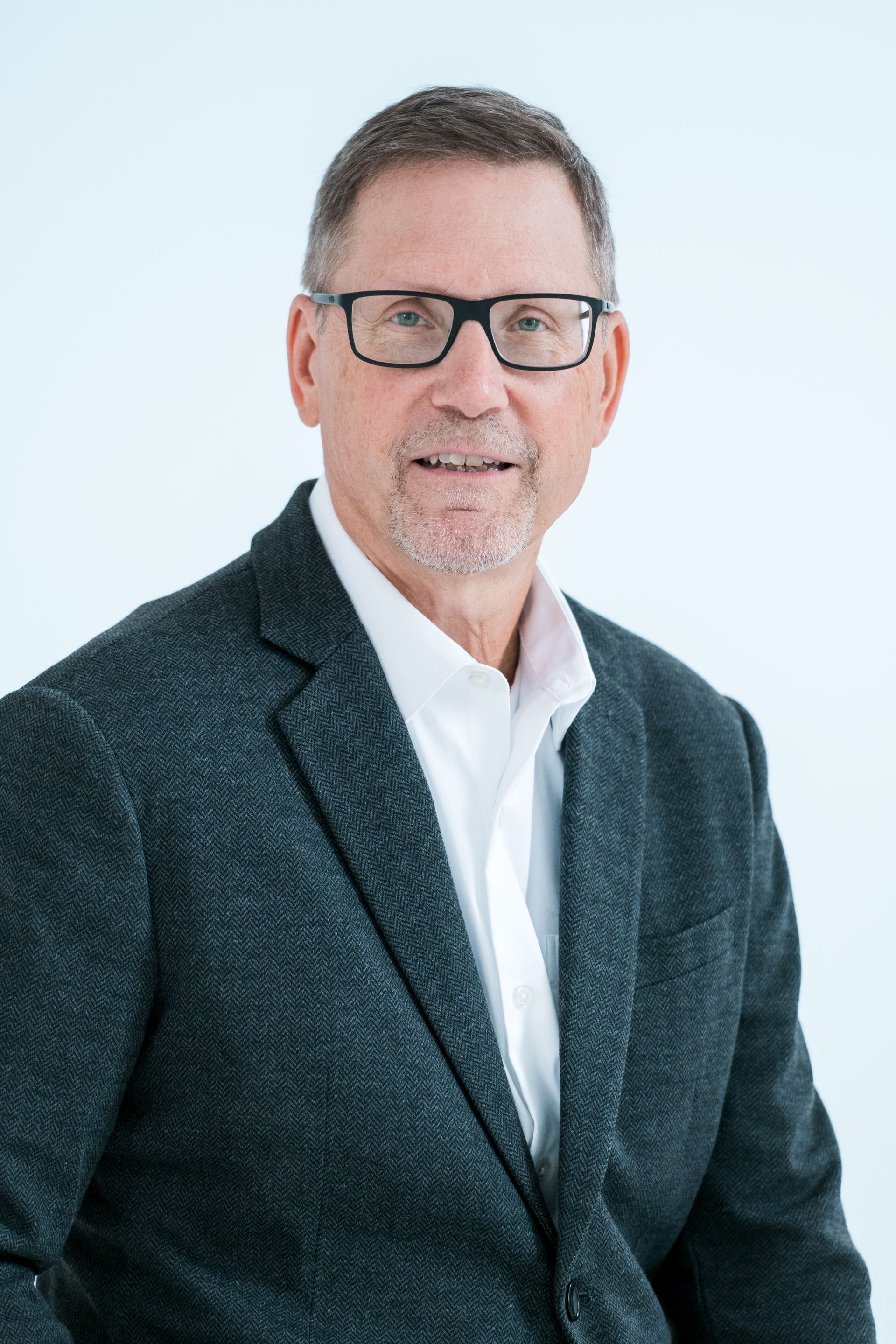 A man wearing glasses and a suit and tie is smiling for the camera.
