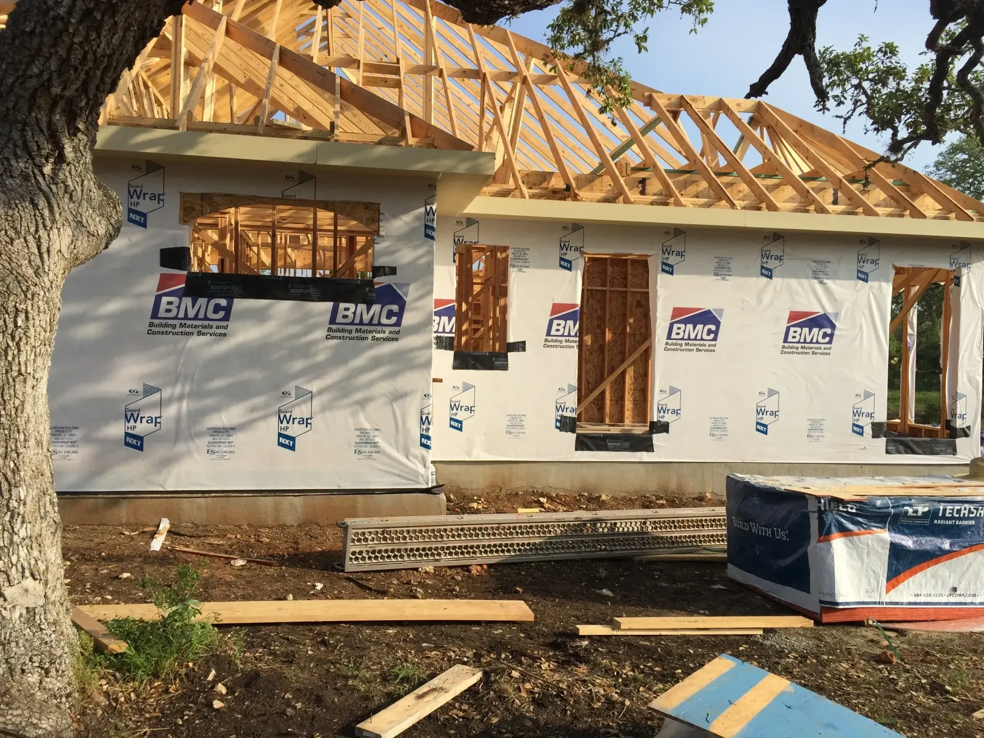 House under construction with wood framing and sheathing, near a tree.