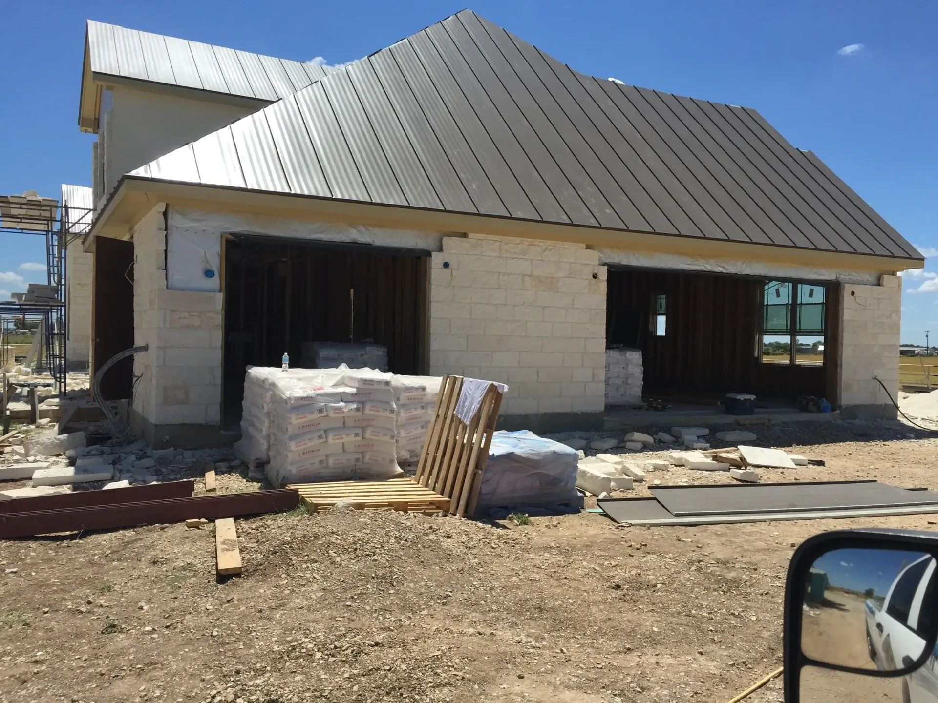 Construction of a home with a metal roof and light-colored brick exterior on a sunny day.