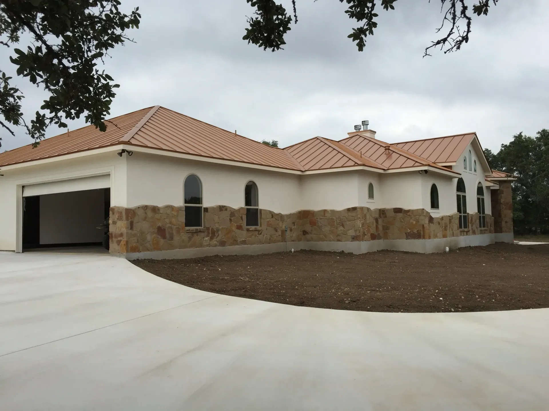 Beige stucco and stone house with red tile roof and attached garage; overcast day.
