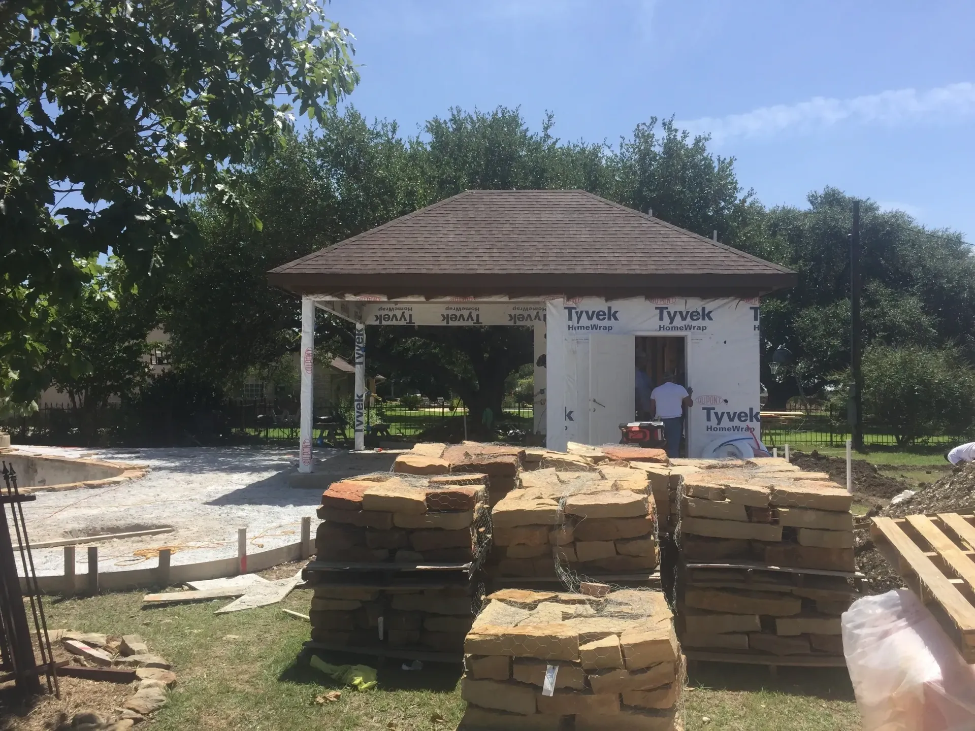 Construction site: building with brown roof and white siding, stacked bricks, blue sky.
