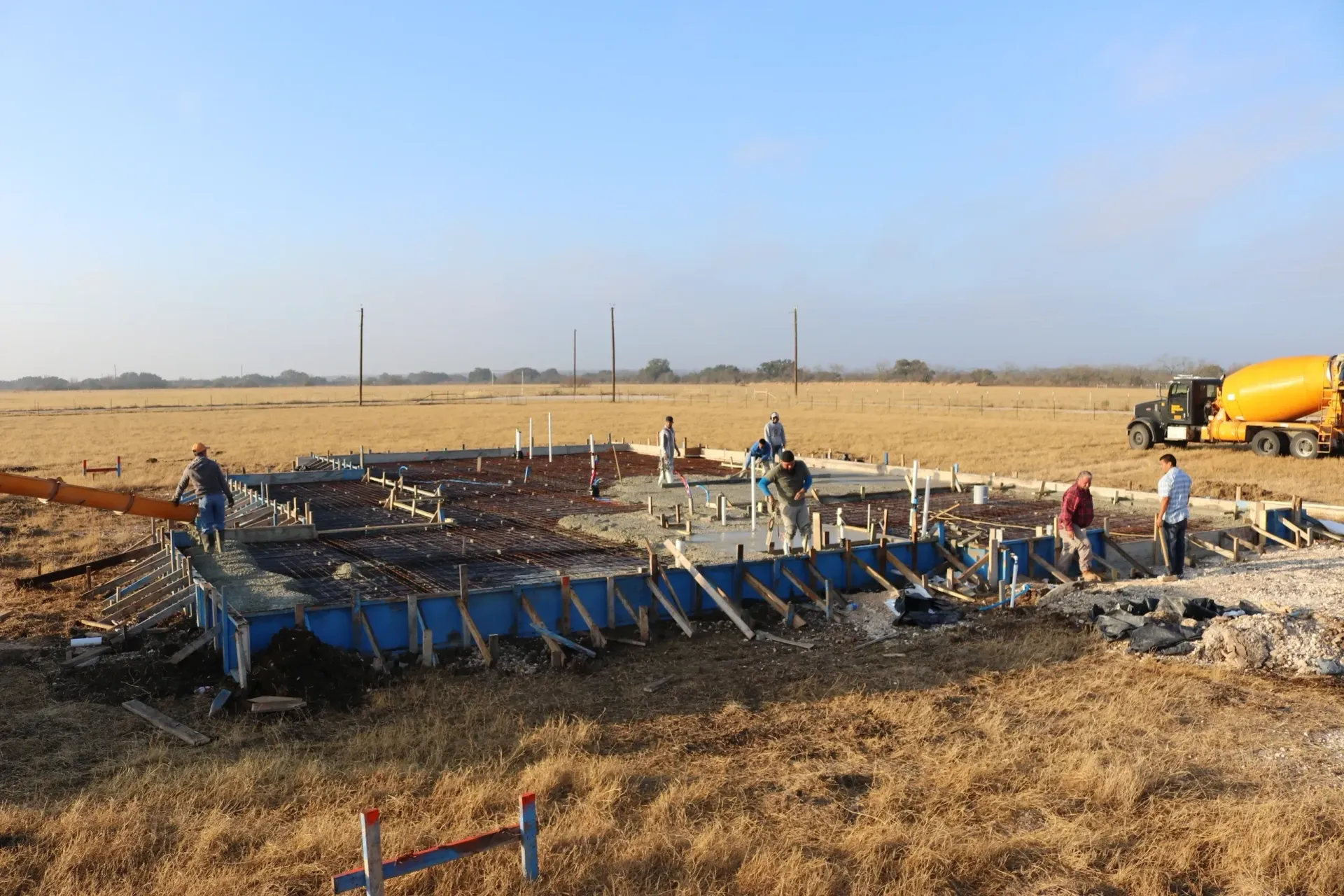 Construction site with a partially built concrete foundation. Workers near concrete truck.