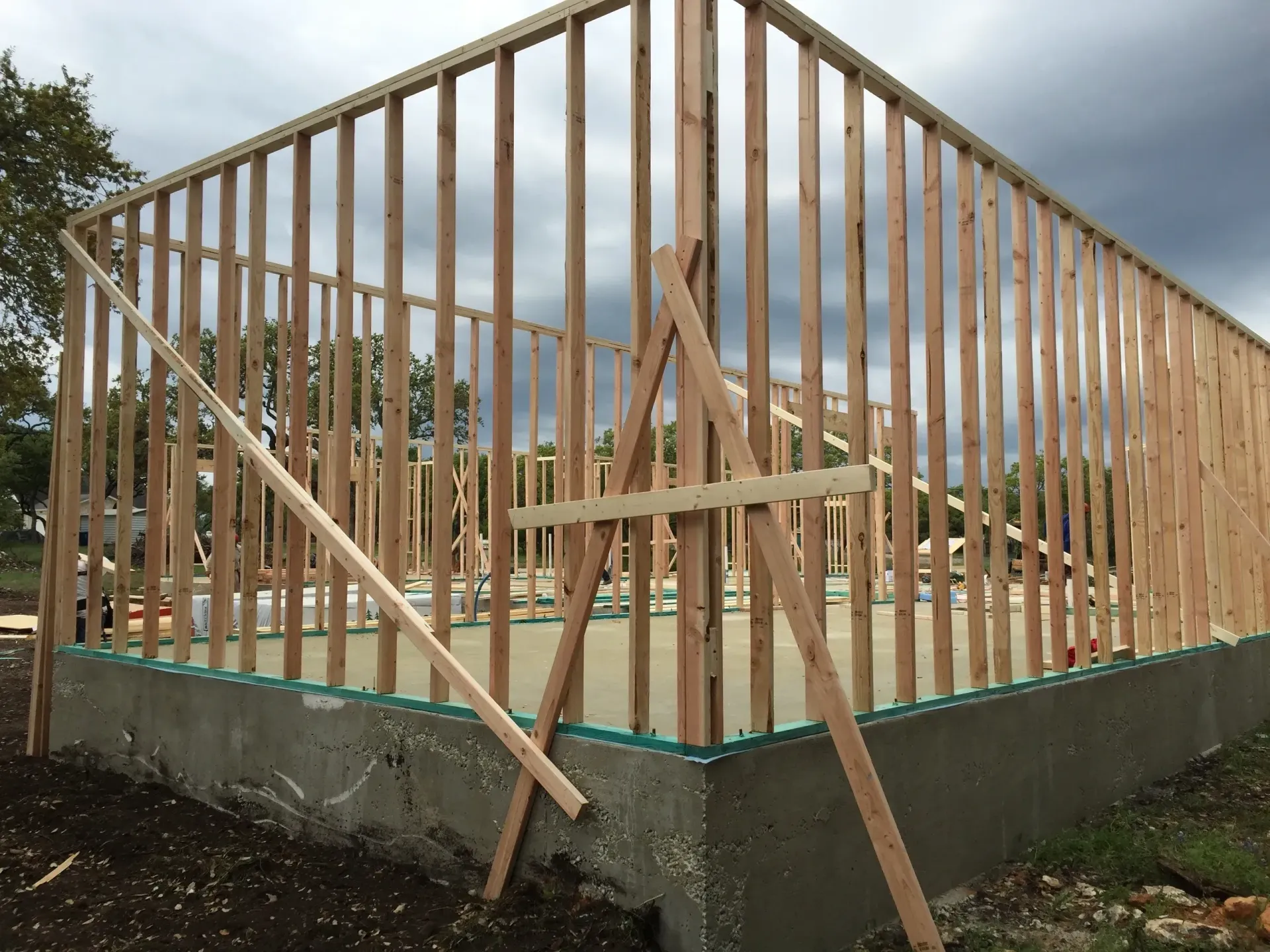 Wooden frame of a building under construction on a concrete foundation, supported by temporary braces.