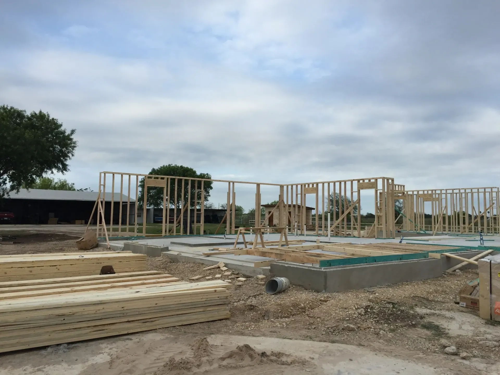 Framing of a building under construction on a concrete foundation, cloudy sky.