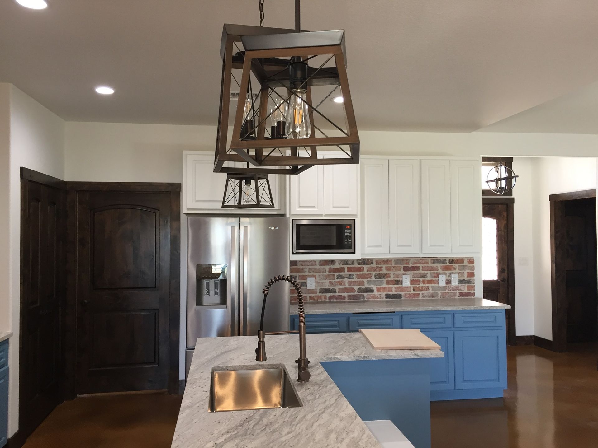 Kitchen with blue island, white cabinets, and brick backsplash, under a wooden chandelier.