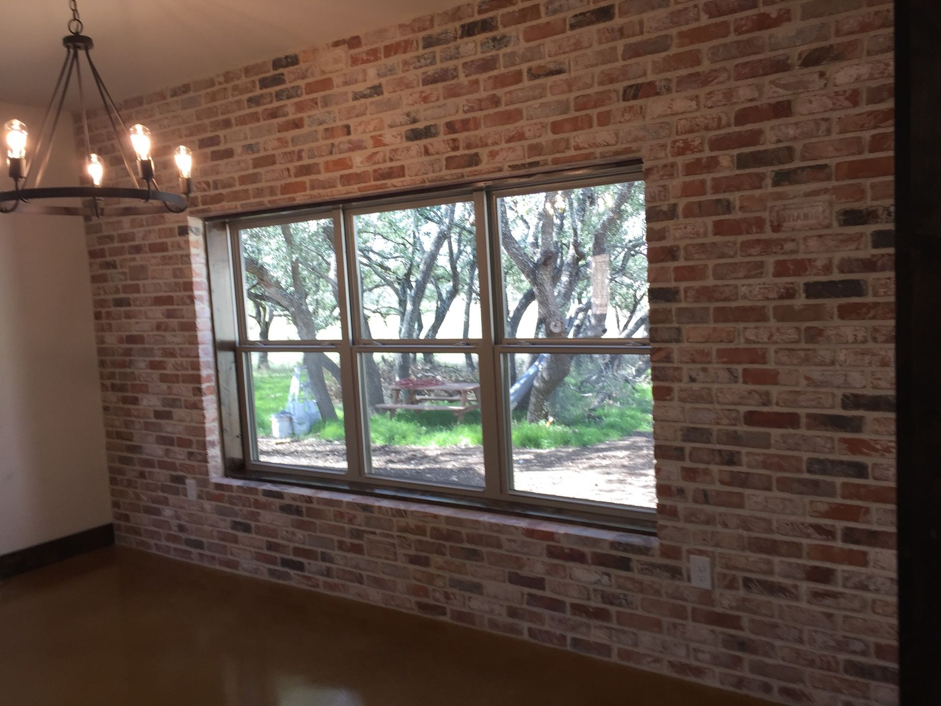 Brick wall interior with window overlooking trees; chandelier hangs above.