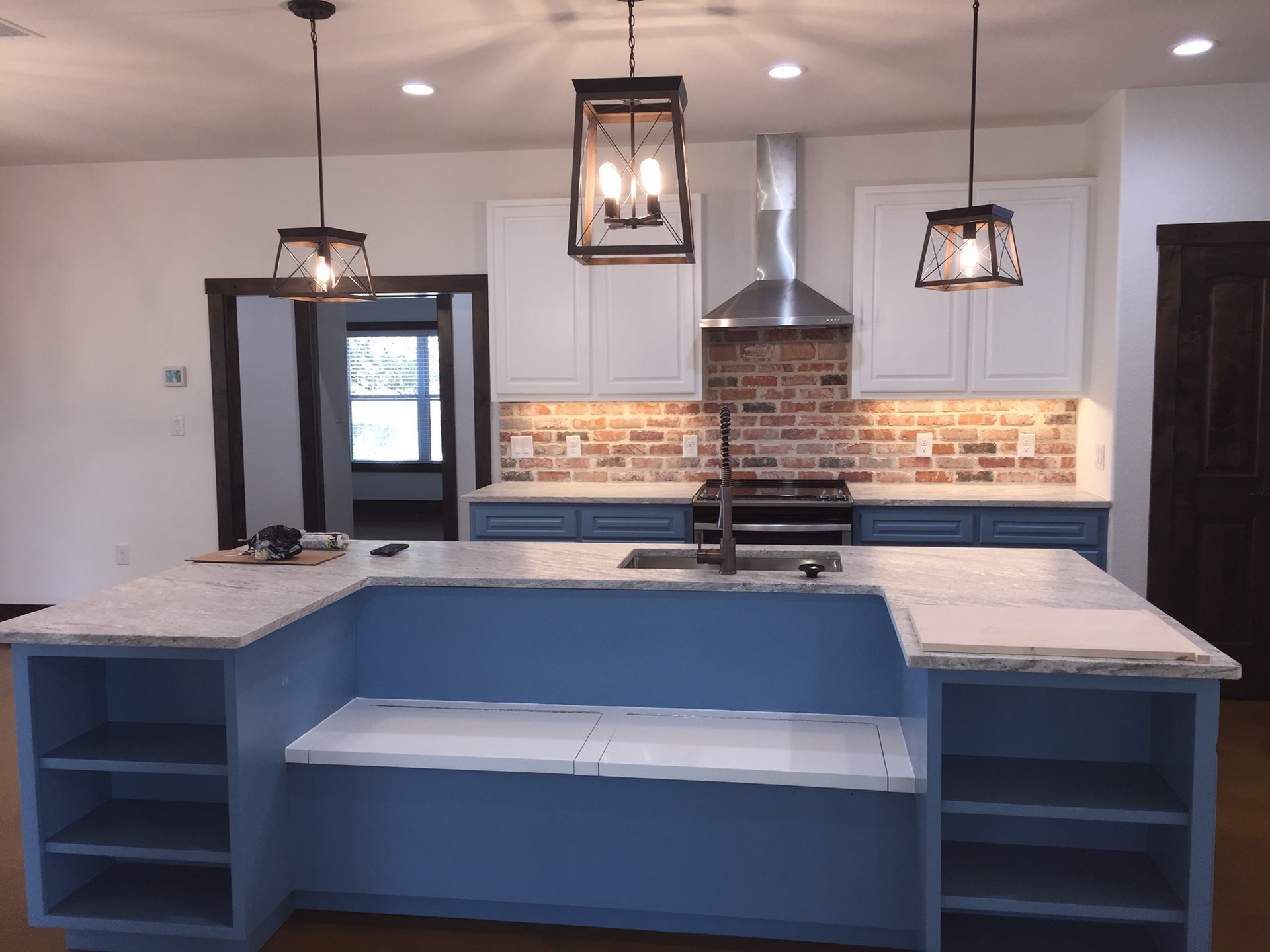 Kitchen with blue island, white countertops, brick backsplash, and hanging black pendant lights.