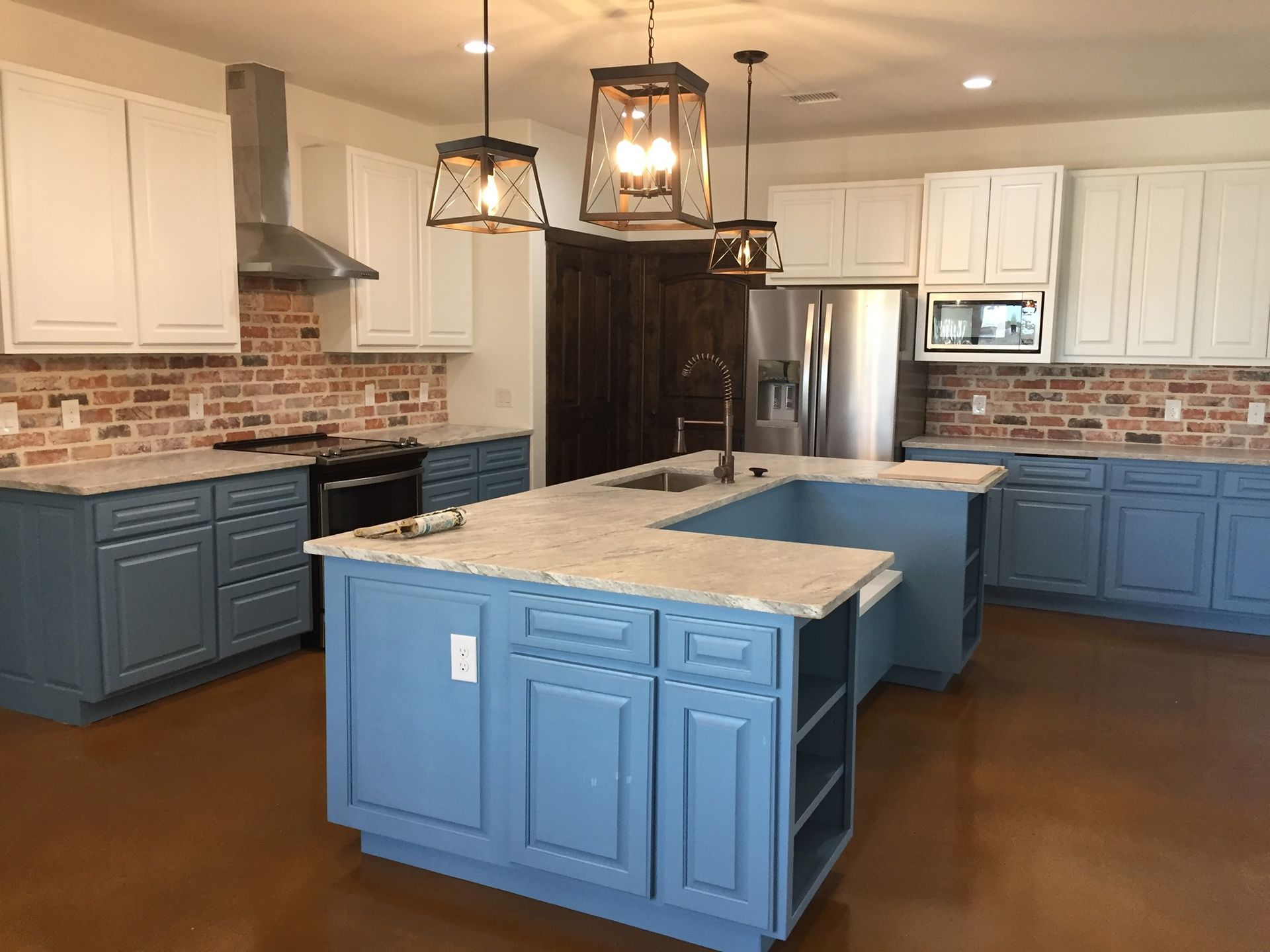 Kitchen with blue and white cabinets, brick backsplash, and large island with granite countertop.