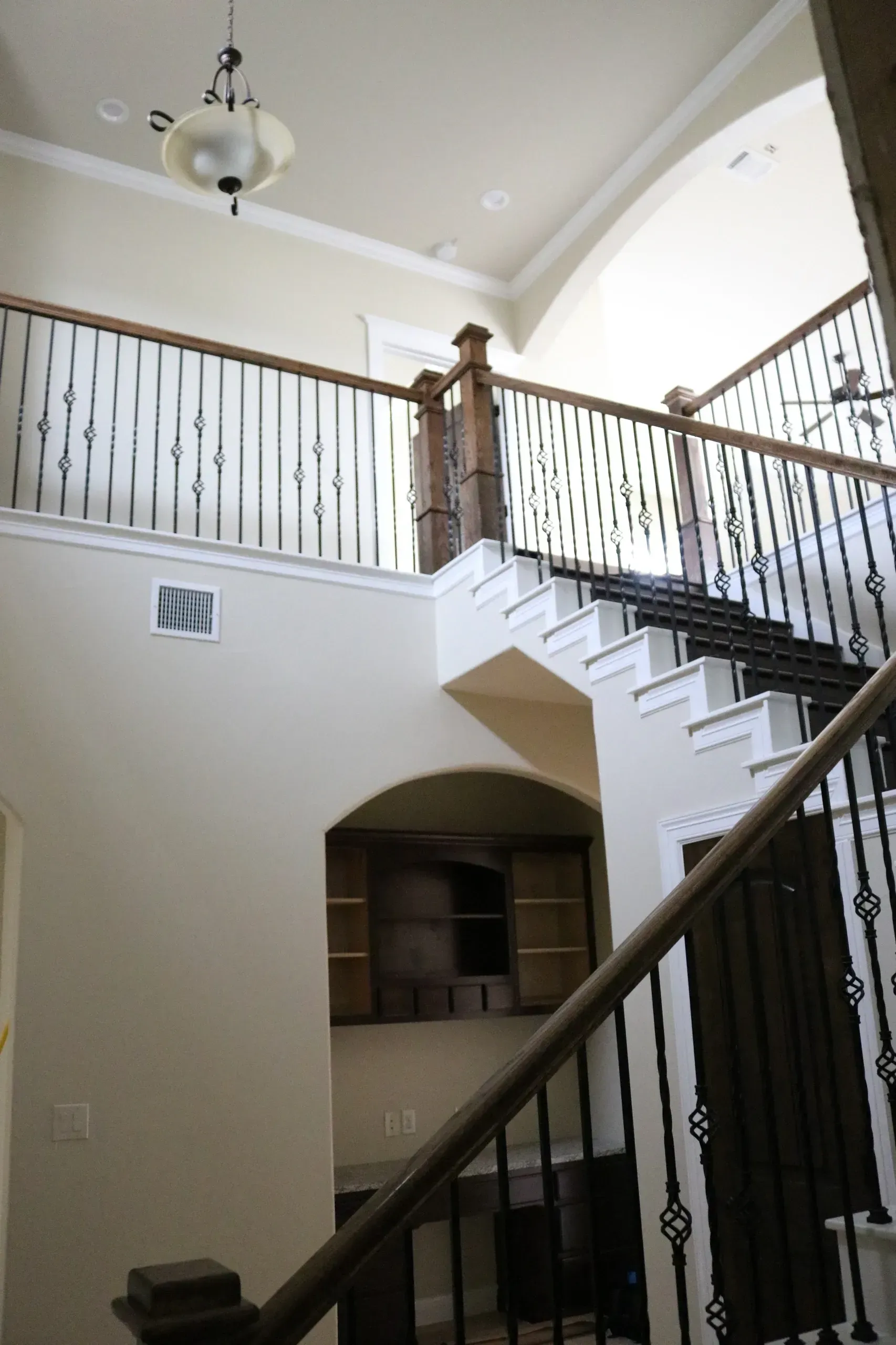 Interior view of a two-story staircase with decorative iron railings and a light fixture.