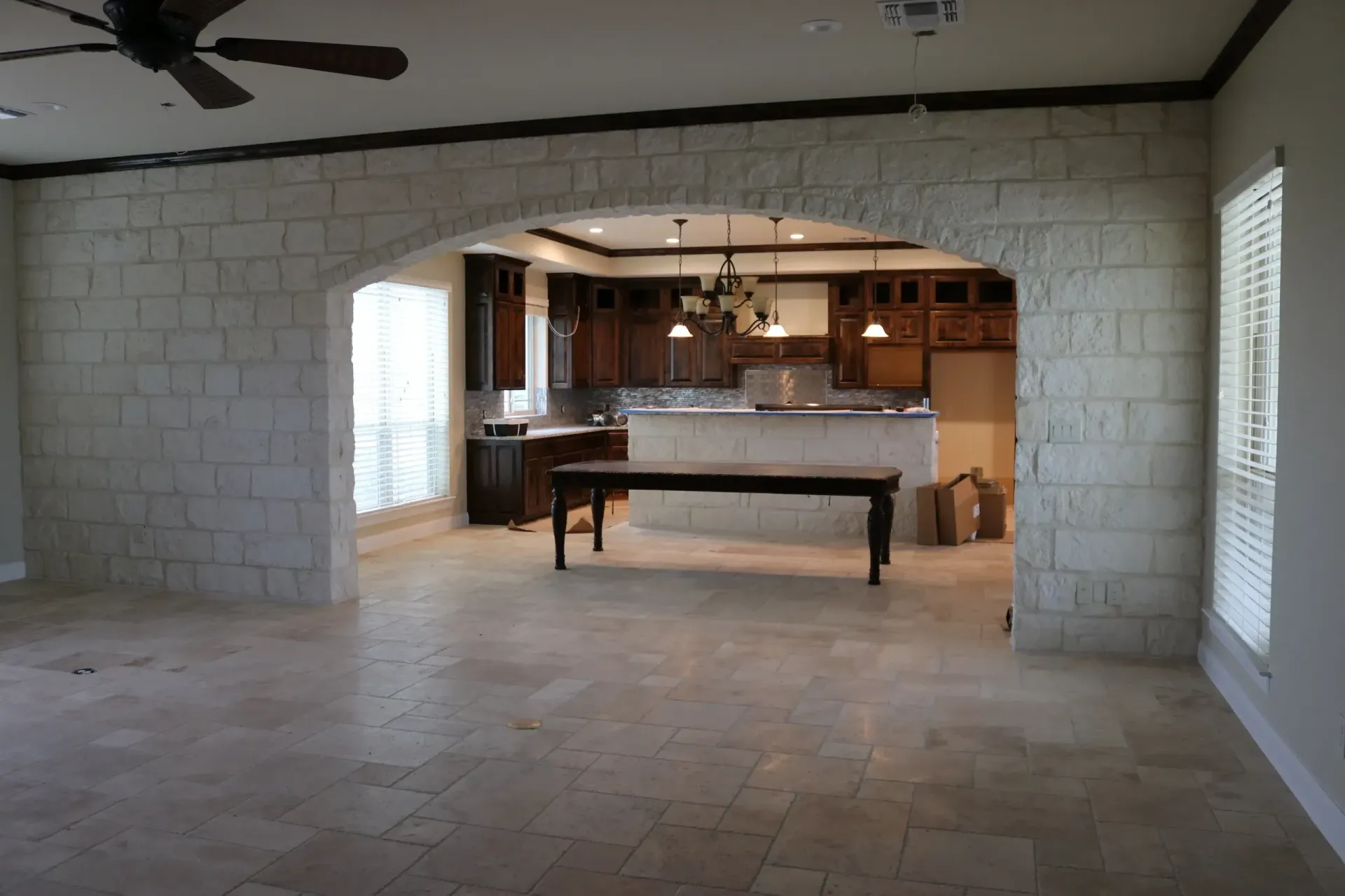 Stone archway leading to a kitchen with dark cabinetry, table, and tiled floor.