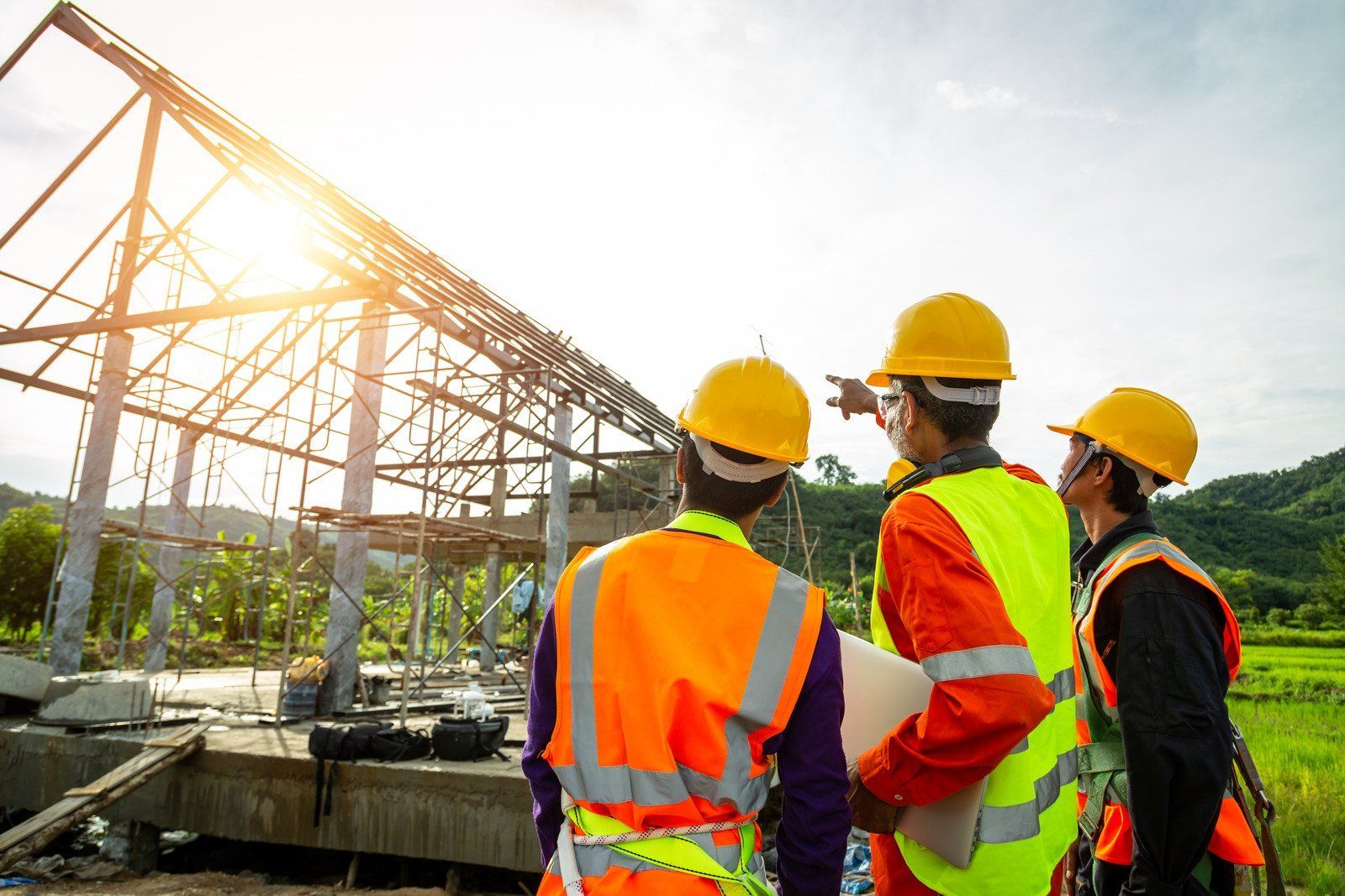 Construction workers in hard hats and vests examining a building frame under the bright sun.
